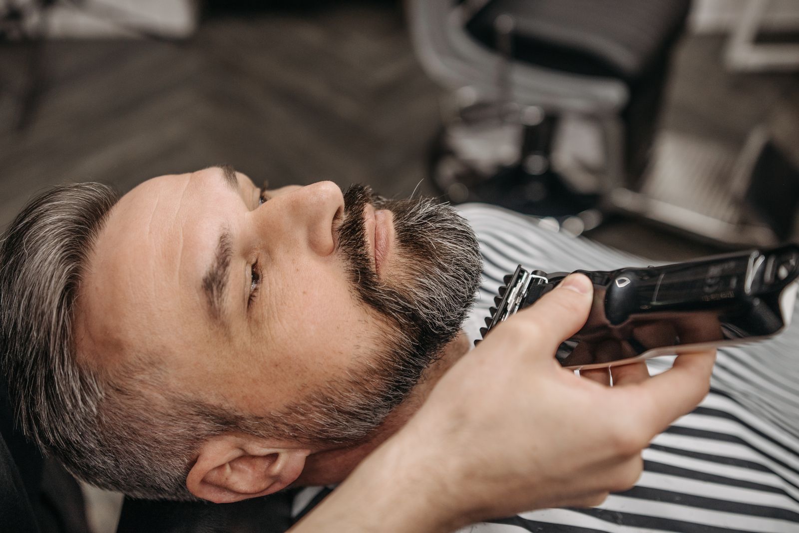 Barberare som trimmar en mans skägg med trimmer